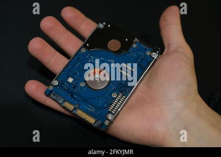 Mano dell'uomo tenere un dispositivo di memorizzazione hdd al buio superficie, componenti tecnici, parti per la sicurezza dei dati Foto Stock