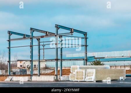 Struttura in metallo di un nuovo edificio moderno in costruzione e pannelli sandwich impaccati in un cantiere. Foto Stock