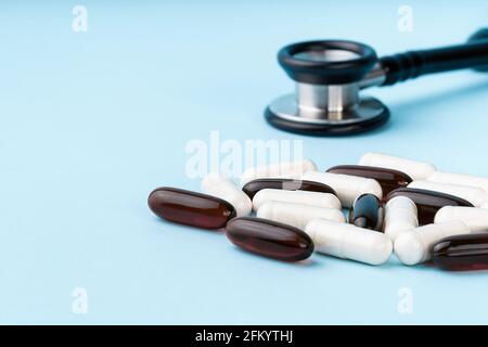 Capsule assortite di colore marrone e bianco, stetoscopio, pillole, isolate su sfondo blu. Integratori nutrizionali per perdita di peso ed energia, aiuti alimentari Foto Stock