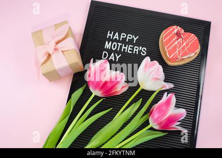 Cartellone nero con lettere bianche in plastica con citazione Happy Mothers Day, su sfondo rosa. Vista dall'alto Foto Stock