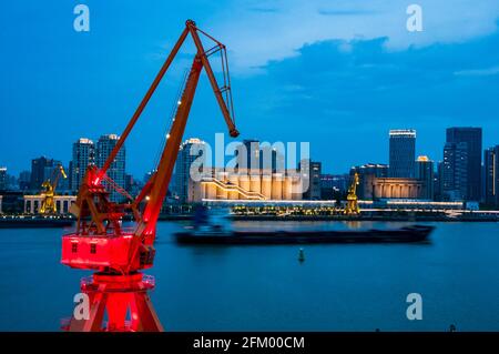 Una vecchia gru di trasporto nel distretto di Yanpu incornicia una barca di carico e gli edifici sul lato di Pudong del fiume Huangpu, Shanghai, Cina. Foto Stock