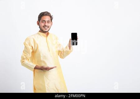 Giovane indiano nella tradizione indossa e mostra lo schermo dello smartphone su sfondo bianco. Foto Stock