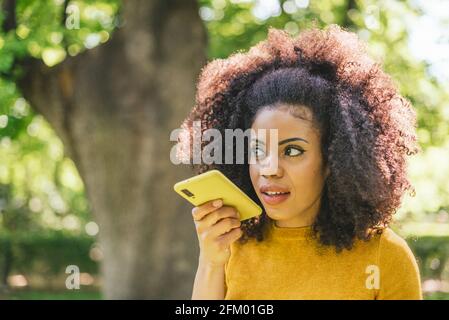 Bella donna afro che invia un messaggio audio sul suo cellulare. Foto Stock