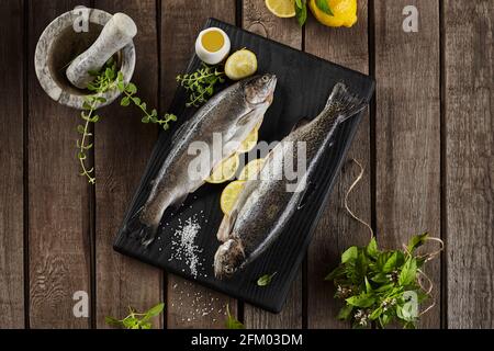 Vista dall'alto di due trote ripiene di limone crudo con erbe su tavola di legno Foto Stock