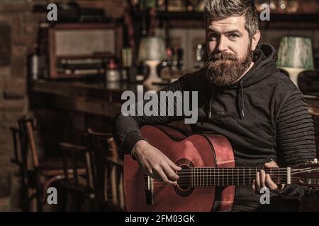 Suona il chitarrista bearded. Uomo bearded che suona la chitarra, tenendo una chitarra acustica tra le mani. Suonare la chitarra. Beard hipster uomo seduto in un pub Foto Stock