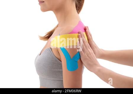 Fisioterapista che ha messo su nastro di chinesio sulla spalla femminile del paziente isolato su sfondo bianco Foto Stock