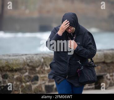 La gente lotta per camminare contro i venti forti in Porthleven, Cornovaglia, Regno Unito Foto Stock