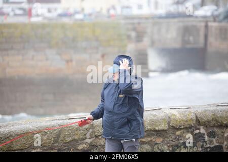 La gente lotta per camminare contro i venti forti in Porthleven, Cornovaglia, Regno Unito Foto Stock