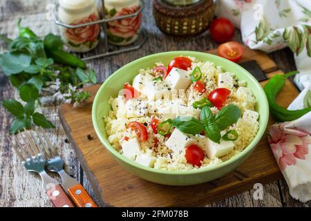 Concetto di dieta alimentare, insalata di tabbouleh. Insalata couscous con formaggio feta, pomodori, basilico e peperoncino su un rustico tavolo di legno. Foto Stock