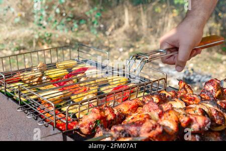 Uomo cucina barbecue all'aperto. Verdure alla griglia e carne sugli spiedini un fuoco aperto. Foto Stock