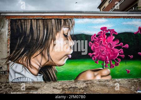 Ein Graffiti an einer alten Mauer zeigt ein Mädchen, welches wie bei einer Pusteblume ein Coronavirus anpustet, welches dann auseinander fliegt. Ein s Foto Stock