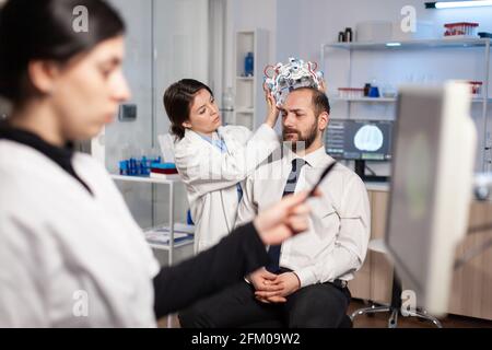 Ricercatore di neurologia che regola le cuffie cerebrali sul paziente durante lo studio, esaminando il sistema nervoso. Sensori per tomografia ad alta tecnologia, medico di neuroscienze. Foto Stock