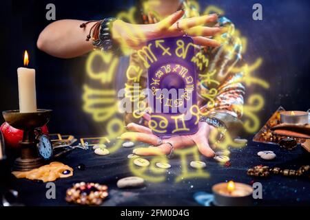 Una cassonatrice di fortuna tiene in mano uno smartphone, da cui partono luminosi cerchi zodiacali. Primo piano. Il concetto di astrologia, magia ed esotericis Foto Stock
