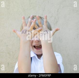 concetto di ritorno a scuola. le parole sono scritte sulle mani di un piccolo scolaro in una camicia bianca sullo sfondo di un muro beige. Prima volta a sc Foto Stock