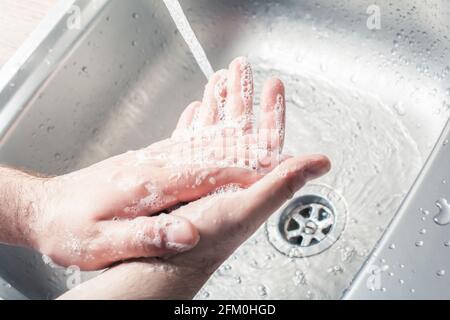 Maschio che gli inzuppava le mani accanto a versare acqua ad A. Lavandino da cucina Foto Stock