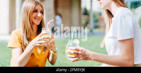 Due donne che si siedono sull'erba con cocktail alla limonata. Foto Stock