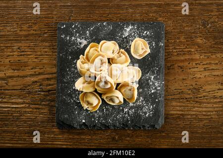 Vista dall'alto della tradizionale pasta italiana di cappelletti fatti a mano su nero tavola cosparsa di farina posta su tavola di legno Foto Stock