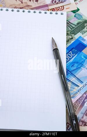 Carta moneta e un foglio bianco. Penna nera e blocco note. Denaro russo e un notebook per le note. Foto Stock