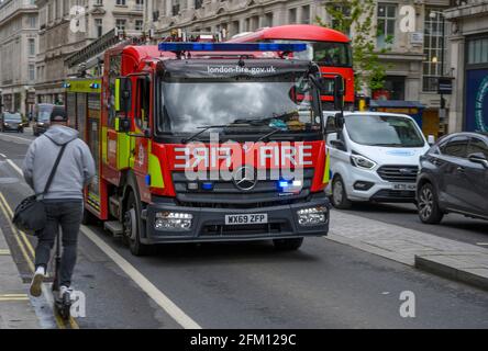 Fire Engine on Emergency Call guida in modo errato lungo Regent Street, oltrepassando la fila del traffico in coda e il pilota di scooter elettrico nel centro di Londra, Regno Unito Foto Stock