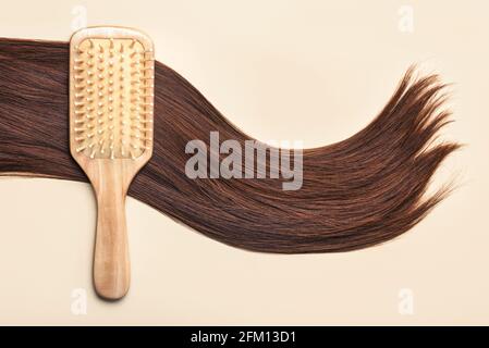 Spazzola per capelli con ciocca di capelli marroni femminili su un beige Background.Hairdresser salone e concetto di acconciature Foto Stock