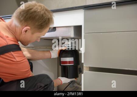 Il lavoratore sta installando un tritadocumenti per rifiuti domestici per il lavello della cucina. Foto Stock