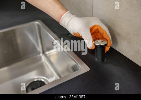 Un idraulico sta impostando il pulsante di avvio del tritadocumenti sul lavandino della cucina. Foto Stock