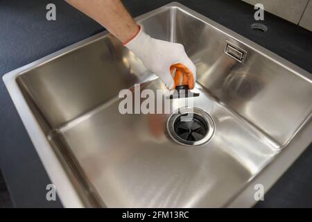 Una mano umana tiene il coperchio della fogna di un tritadocumenti da cucina. Foto Stock