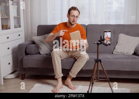 Bel blogger uomo a casa presenta libro mentre video stream. Social media marketing e vendite online Foto Stock