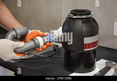 Un lavoratore sta installando un tritatutto per rifiuti domestici per il lavandino della cucina. Foto Stock