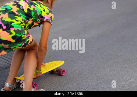 Defocalizzare la bambina urbana con uno skateboard giallo. Bambini in giro nel parco a bordo di uno skateboard. Stile cittadino. Bambini urbani. Il bambino impara a guidare un Foto Stock