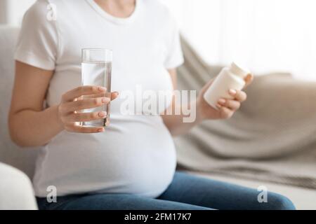 Donna incinta vasetto da presa con vitamine Prenatali e bicchiere d'acqua, tagliato Foto Stock