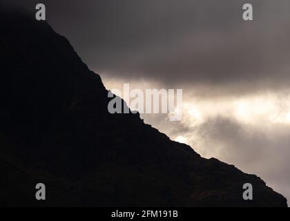 Drammatica luce del cielo proveniente dalle tenebre mentre il sole si rompe attraverso la nuvola bassa dietro il suggestivo monte Snowden nel Galles del Nord Snowdonia. Roccia frastagliata Foto Stock