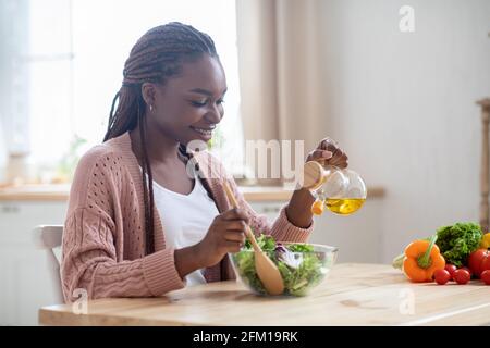 Felice giovane donna nera preparare insalata di verdure in cucina Foto Stock