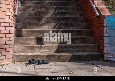 Un paio di scarpe nere gettate sul fondo di un volo di scalini di cemento vicino al centro città, Northampton, Inghilterra, UK. Foto Stock