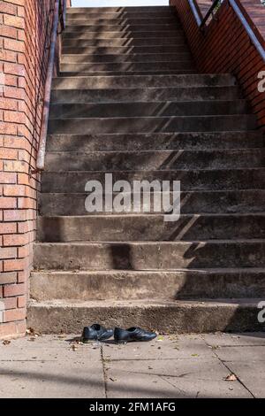 Un paio di scarpe nere gettate sul fondo di un volo di scalini di cemento vicino al centro città, Northampton, Inghilterra, UK. Foto Stock