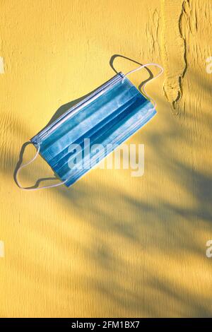 Maschera protettiva monouso blu contro Coronavirus Covid 19 su sfondo giallo. Concetto di protezione, prevenzione Foto Stock