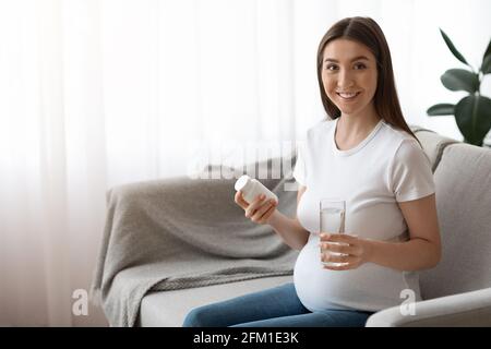 Vitamine prenatali. Donna incinta vasetto di tenuta con pillole e bicchiere d'acqua Foto Stock