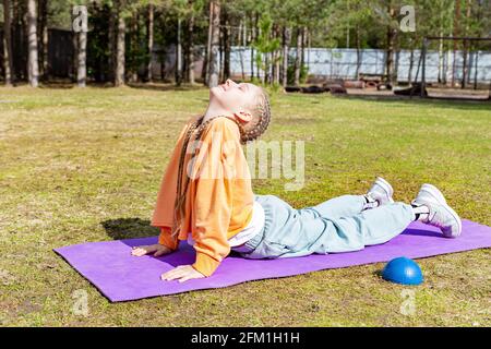 La ragazza adolescente pratica yoga in natura in una giornata estiva su un tappetino sportivo, si allunga Foto Stock