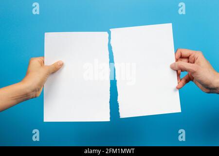 Mani di capretto e donna che tengono i pezzi di carta bianca strappata foglio su sfondo azzurro Foto Stock