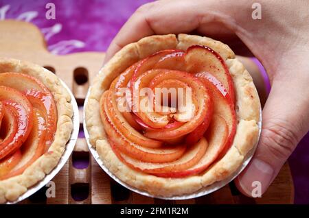 Mani dell'uomo che mettono una deliziosa rosa di mela appena sfornata tartlet sulla tavola di legno Foto Stock