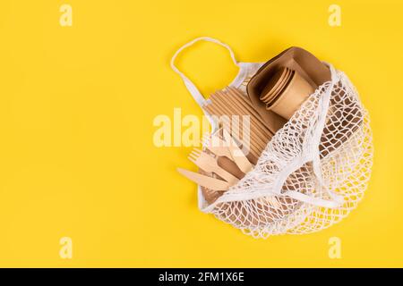 Vasetti e contenitori di carta Kraft con posate in legno in sacchetto di rete di cotone su sfondo giallo con spazio copia, stoviglie eco-compatibili . Cibo di strada Foto Stock