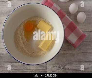 Ingredienti per preparare una torta in una ciotola di smalto bianco. Vista dall'alto sullo sfondo di un tavolo in legno Foto Stock