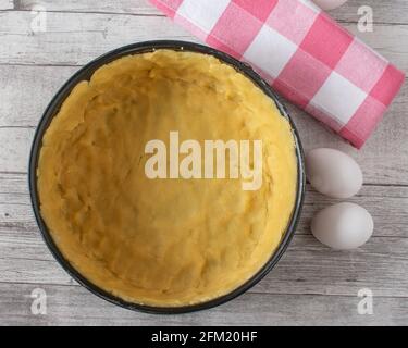 pasta fresca fatta in casa per preparare una base di torta in un teglia rotonda su fondo tavola di legno dall'alto Foto Stock