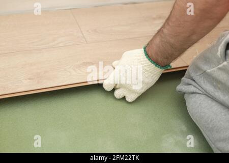 Installazione di pavimenti in laminato o parquet in camera, dettaglio su mani di uomo che si inserisce piastrelle di legno, su base di schiuma verde. Foto Stock