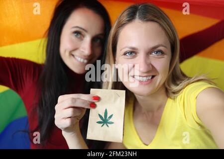 Due donne sorridenti che tengono bandiera lgbt e pacchetto di marijuana Foto Stock