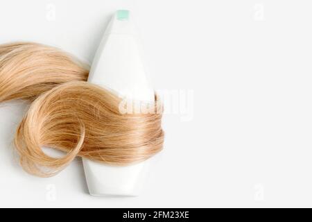 Shampoo o flacone di balsamo avvolto in ciocca di capelli biondi ricci isolati su sfondo chiaro, vista dall'alto. Disposizione piatta, spazio di copia per il testo. Cura dei capelli Foto Stock