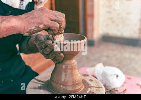 Vecchio maestro di ceramica scolpendo le stoviglie in argilla con le mani. Primo piano di messa a fuoco selettiva Foto Stock