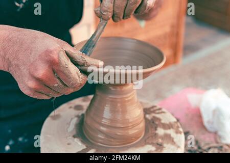 Vecchio maestro di ceramica scolpendo le stoviglie in argilla con le mani. Primo piano di messa a fuoco selettiva Foto Stock