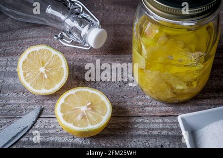 Liquore al limoncello ingredienti: Scorza di limone infusa in un vasetto di alcool circondato da una bottiglia, un taglio di limone a metà e zucchero Foto Stock