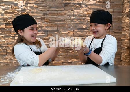 Bambini felici e sorridenti che tengono un gnocco nei vestiti dello chef Foto Stock